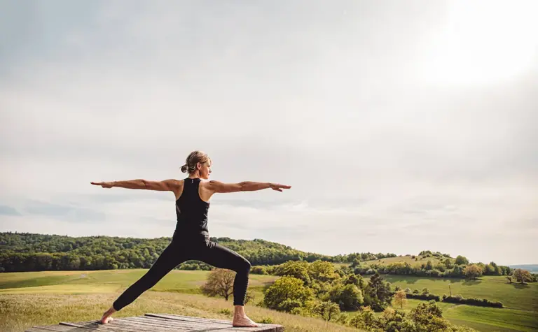 Yoga-Haltung Krieger im Freien vor grüner Landschaft