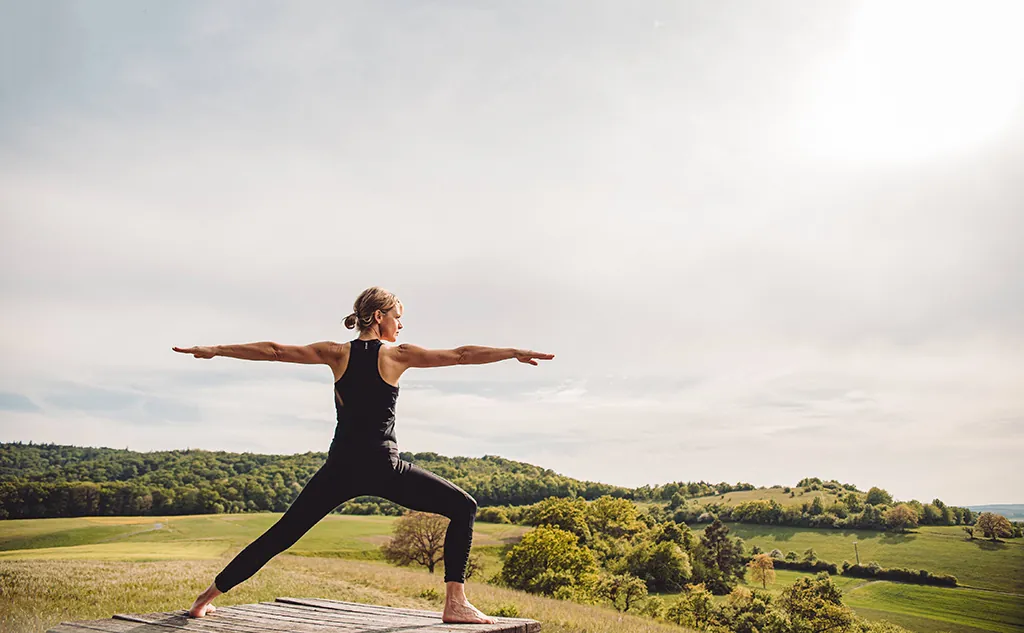 Yoga-Haltung Krieger im Freien vor grüner Landschaft