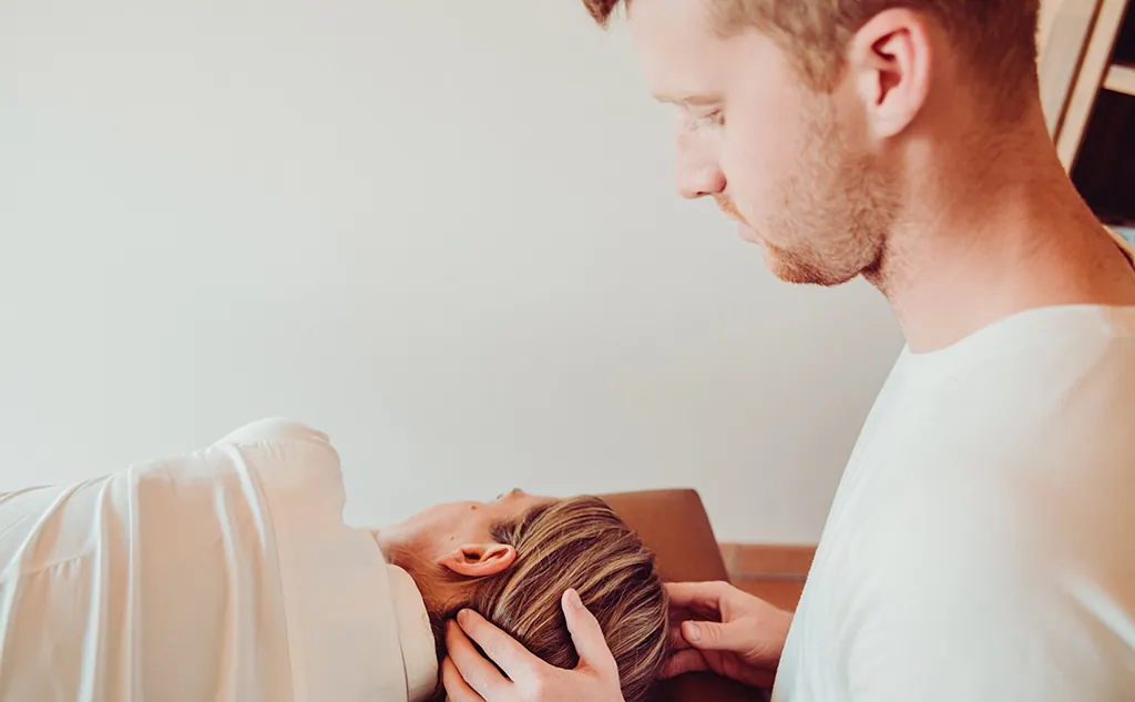 Physiotherapeut behandelt mit den Händen den Nacken einer liegenden Patientin